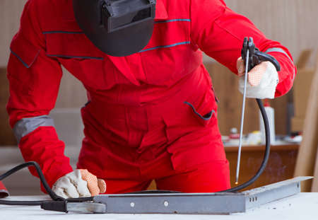 Young repairman with a welding gun electrode and a helmet weldin