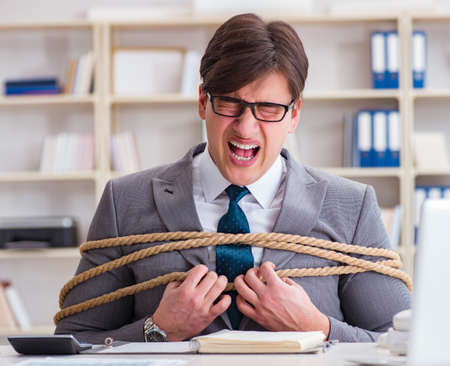 Businessman tied up with rope in officeの写真素材