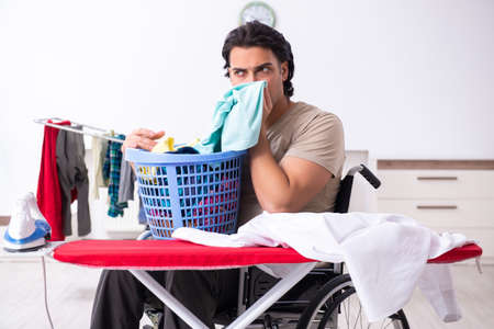 Young man in wheel-chair doing ironing at homeの写真素材