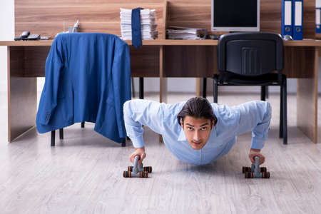 Young handsome businessman doing exercises at workplaceの写真素材