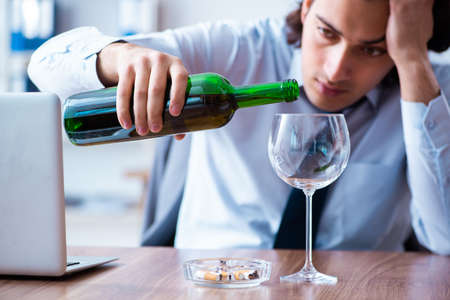 Male employee drinking alcohol and smoking cigarettes at workplaの写真素材