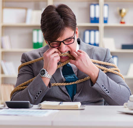 Businessman tied up with rope in officeの写真素材