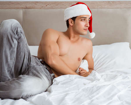 Young sexy man wearing santa hat in bedの写真素材