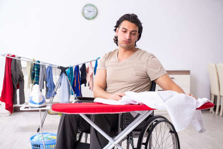 Young man in wheel-chair doing ironing at homeの写真素材
