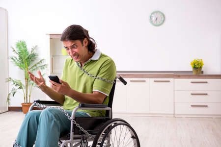 Young male invalid in wheel-chair suffering at home