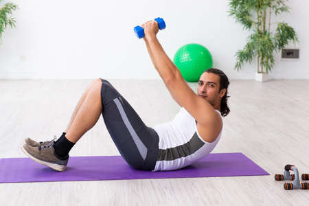 Young handsome man doing sport exercises indoors