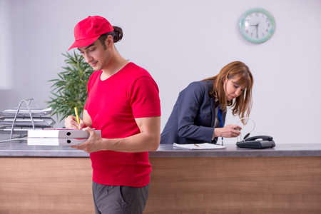 Young male courier delivering pizza to hotels receptionの写真素材
