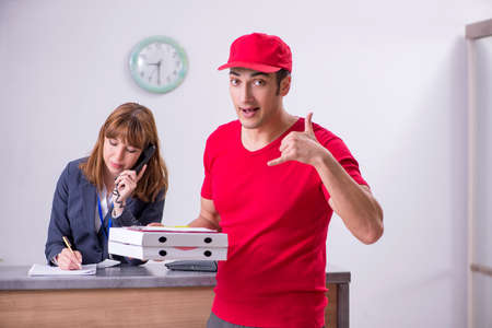Young male courier delivering pizza to hotels receptionの写真素材