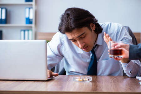 Male employee drinking alcohol and smoking cigarettes at workplaの写真素材