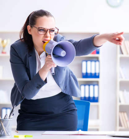 Angry businesswoman yelling with loudspeaker in officeの写真素材
