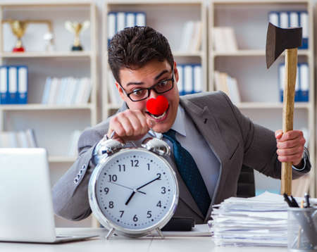 Clown businessman in the office with an axe and an alarm clockの写真素材