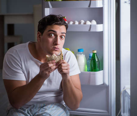 Man at the fridge eating at nightの写真素材