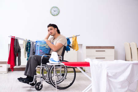 Young man in wheel-chair doing ironing at homeの写真素材