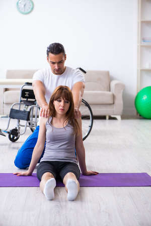 Male physiotherapist doing exercises with injured woman on floorの写真素材