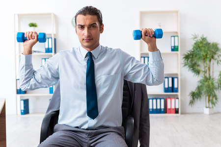 Young handsome employee doing sport exercises at workplaceの写真素材