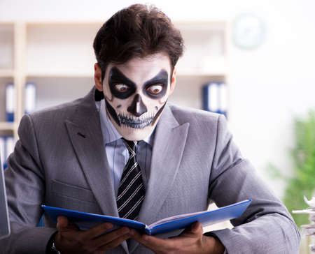 Businessman with scary face mask working in officeの写真素材