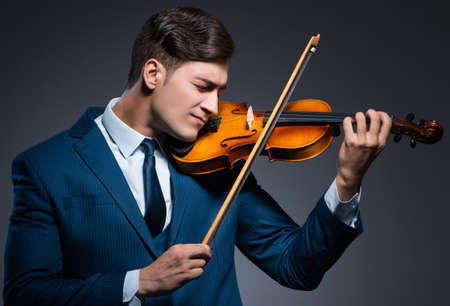 Young man playing violin in dark roomの写真素材