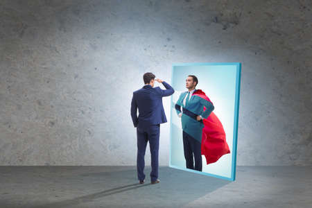 Businessman seeing himself in mirror as superheroの写真素材