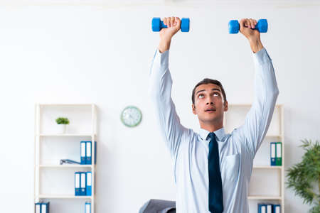 Young handsome employee doing sport exercises at workplaceの写真素材