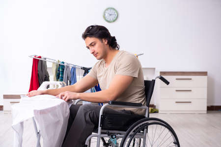 Young man in wheel-chair doing ironing at homeの写真素材