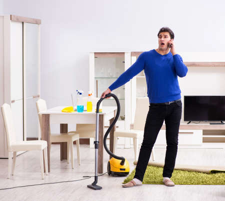 Young man vacuum cleaning his apartmentの写真素材