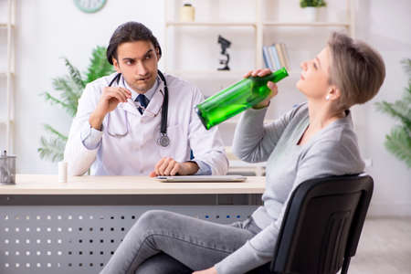 Female alcoholic visiting young male doctorの写真素材