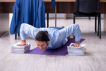 Young handsome businessman doing exercises at workplace