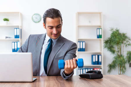 Young handsome employee doing sport exercises at workplaceの写真素材