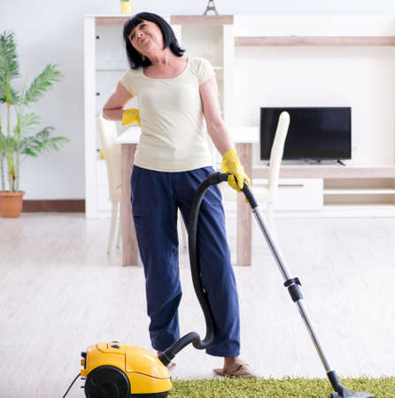 Senior old woman tired after vacuum cleaning houseの写真素材