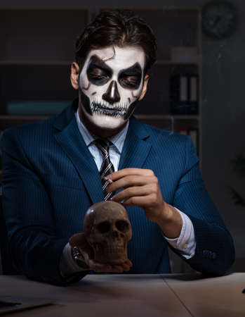 Businessman with scary face mask working late in officeの写真素材