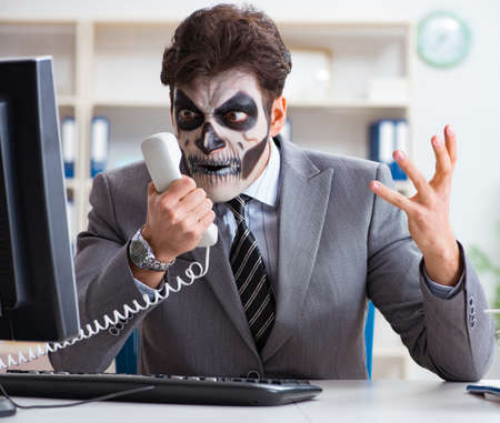 Businessmsn with scary face mask working in officeの写真素材