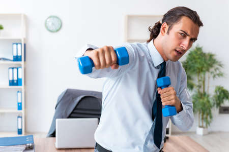 Young handsome employee doing sport exercises at workplaceの写真素材