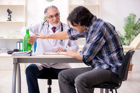 Young male alcoholic visiting old doctorの写真素材
