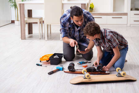 Young father repairing skateboard with his son at homeの写真素材