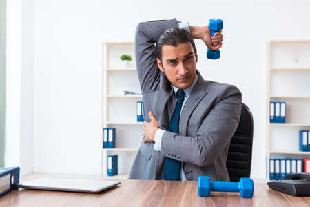 Young handsome employee doing sport exercises at workplaceの写真素材