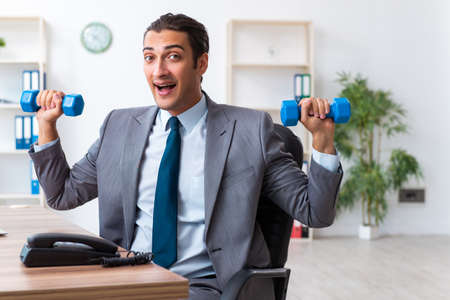 Young handsome employee doing sport exercises at workplaceの写真素材