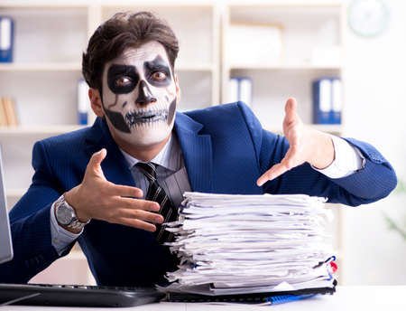 Businessmsn with scary face mask working in officeの写真素材
