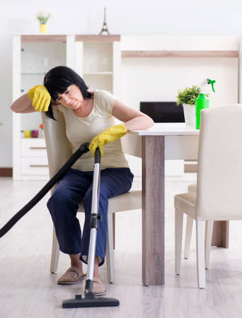 Senior old woman tired after vacuum cleaning houseの写真素材