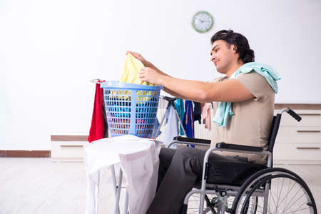 Young man in wheel-chair doing ironing at homeの写真素材