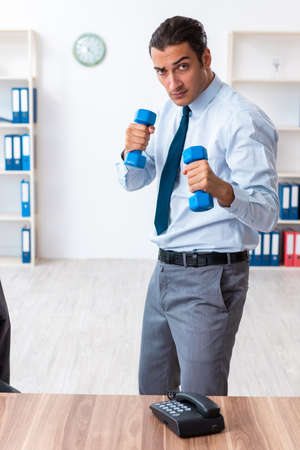 Young handsome employee doing sport exercises at workplaceの写真素材