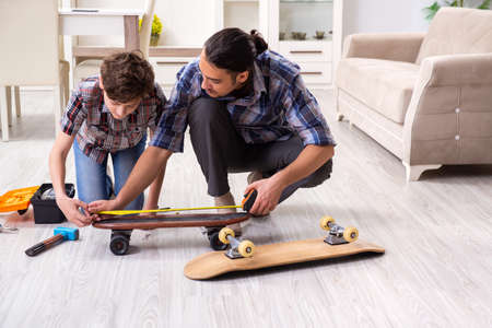 Young father repairing skateboard with his son at homeの写真素材
