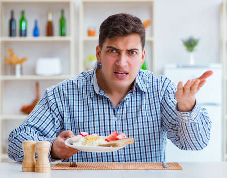 Young husband eating tasteless food at home for lunchの写真素材