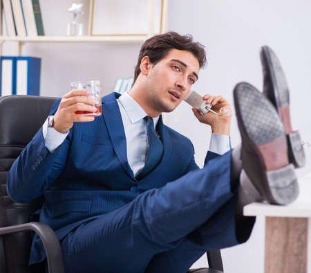 Young businessman employee drinking in the office at deskの写真素材