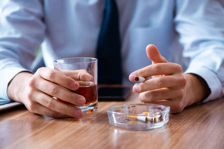 Male employee drinking alcohol and smoking cigarettes at workpla