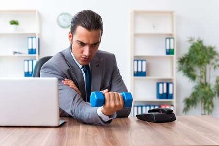 Young handsome employee doing sport exercises at workplaceの写真素材