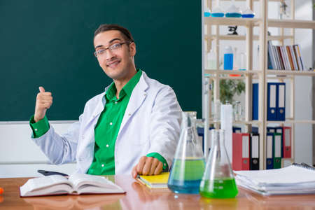 Young male chemist teacher in front of blackboard