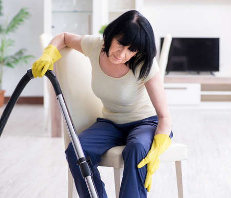Senior old woman tired after vacuum cleaning houseの写真素材