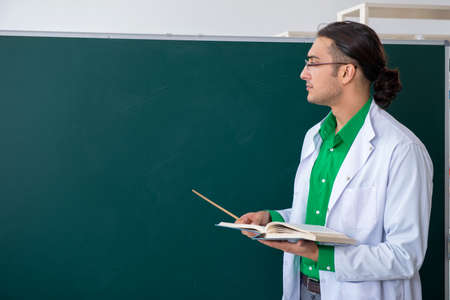Young male chemist teacher in front of blackboardの写真素材