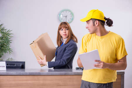Young male courier delivering box to hotels receptionの写真素材