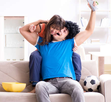Young man watching football with his wife at homeの写真素材